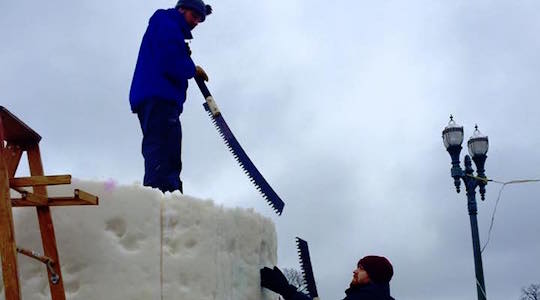Two people with saws near a large snow cylinder